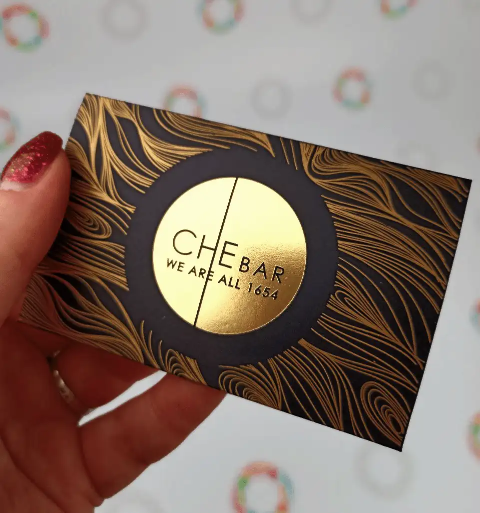 Black envelope with a gold logo and a bronze pattern in a woman's hand, front view